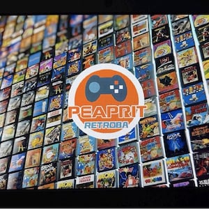 May include: A digital screen displaying a grid of numerous colorful retro video game cartridge labels. Centered on the screen is a circular white logo featuring a blue game controller icon above the orange text PEAPRIT and blue text RETROBA.