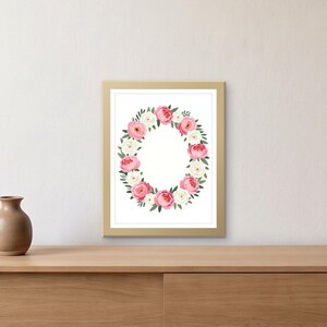 May include: A rectangular wall art print in a gold frame featuring a central oval wreath composed of pink and white peony flowers with green leaves on a white background. The floral arrangement is symmetrical and centered within the frame.