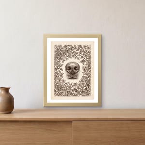 May include: A framed art print featuring a detailed brown ink illustration of a dog nose centered within a dense botanical wreath of flowers, leaves, and small insects. The artwork is encased in a simple gold frame with a white mat border.