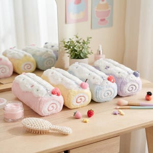 Op de afbeelding: Een collectie van vier pluche, cilindervormige etuis ontworpen als Zwitserse roombroodjes. Elk etui heeft een zachte, pluizige textuur, een ritssluiting en een klein decoratief fruitaccent aan de bovenkant in roze, geel, blauw en paars.