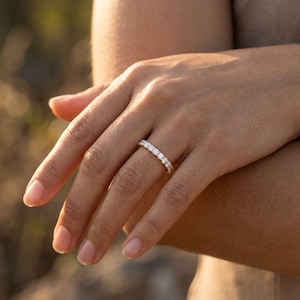 Könnte beinhalten: Ein goldener Eternity-Ring mit einer durchgehenden Reihe kleiner, runder, klarer Edelsteine im Brillantschliff, die in einer gemeinsamen Krappenfassung gefasst sind. Das Metallband hat eine polierte Oberfläche und reflektiert das Licht.