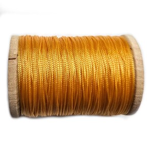 May include: A spool of golden yellow thread wound tightly around a cylindrical wooden core. The thread has a smooth, slightly reflective texture and is wrapped in a continuous, uniform pattern across the entire length of the wooden spool.