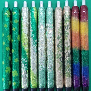 May include: Ten glitter pens with different designs. The pens have a clear plastic body and a black cap. The glitter designs include green shamrocks, green and gold glitter, and a rainbow.