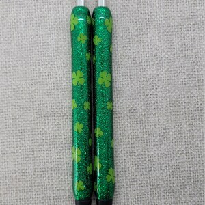 May include: Two green glitter pens with silver accents and a four-leaf clover pattern.