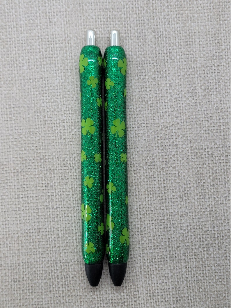 May include: Two green glitter pens with silver accents and a four-leaf clover pattern.