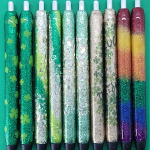May include: Ten glitter pens with different designs. The pens have black caps and silver accents. The designs include green shamrocks, green and silver glitter, iridescent glitter, gold glitter, and rainbow glitter.