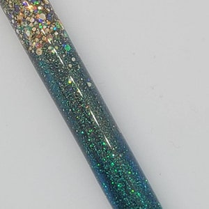 May include: A close-up of a green and gold glitter pen. The pen has a gradient of glitter, starting with gold at the top and fading to green at the bottom.
