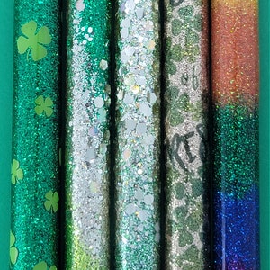 May include: Five glitter-filled tubes with different designs. The first tube is green with shamrock patterns. The second tube is silver with green glitter. The third tube is green with silver glitter. The fourth tube is silver with a shamrock pattern. The fifth tube is a gradient of orange, yellow, green, blue, and purple.