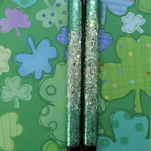 May include: Two green glitter pens with silver glitter accents. The pens have a black ink tip and a silver metal top.