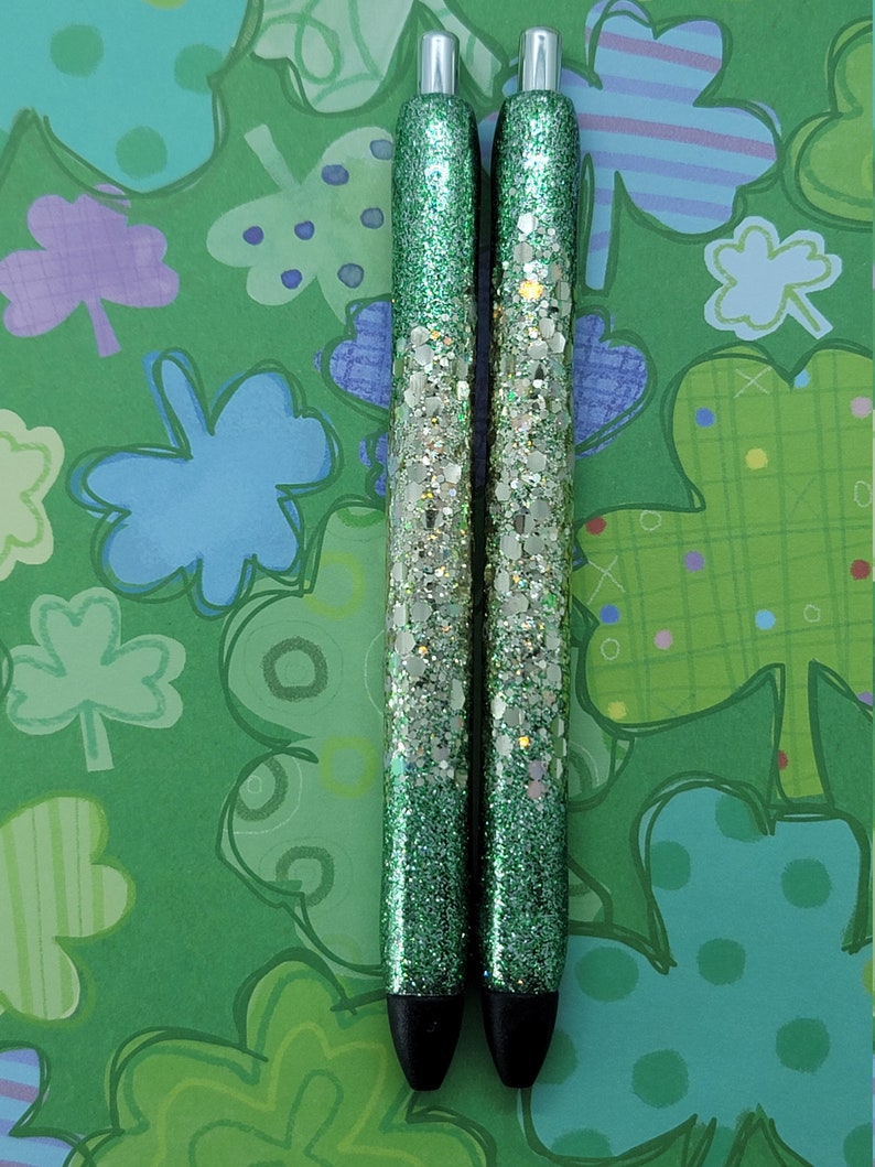 May include: Two green glitter pens with silver glitter accents. The pens have a black ink tip and a silver metal top.