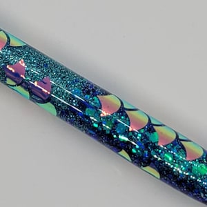 May include: A blue and green glitter pen with iridescent mermaid scales. The pen has a clear body and is filled with blue and green glitter.