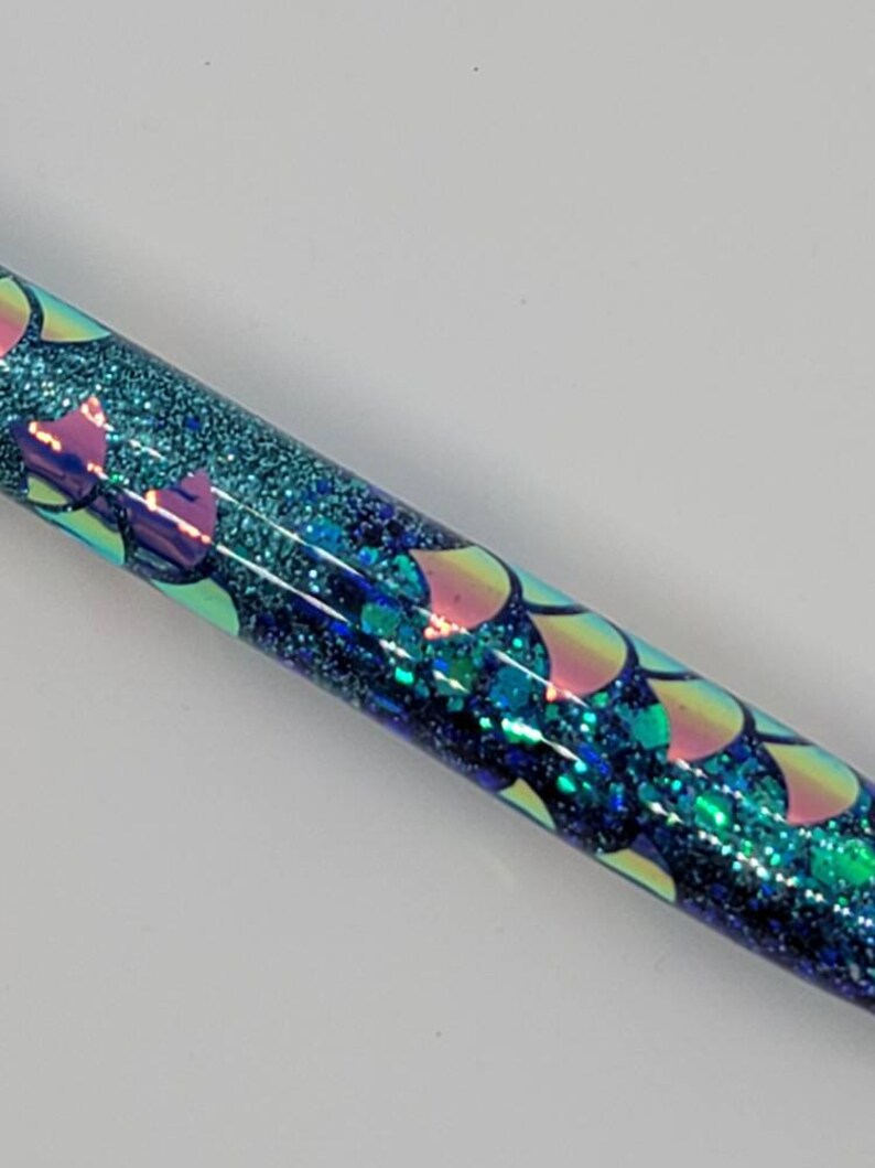 May include: A blue and green glitter pen with iridescent mermaid scales. The pen has a clear body and is filled with blue and green glitter.