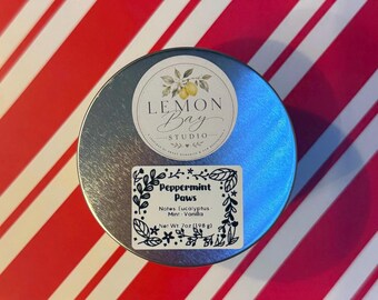 Könnte beinhalten: Eine runde silberne Metalldose mit zwei Etiketten. Das obere runde Etikett zeigt eine Zitronenillustration und den Text Lemon Bay Studio. Das rechteckige Etikett darunter trägt die Aufschrift Peppermint Paws, Notes Eucalyptus, Mint, Vanilla, Net Wt. 7oz (198 g).