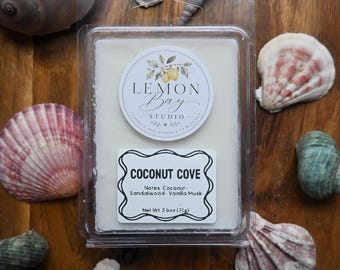 Könnte beinhalten: Ein rechteckiges, weißes Duftwachs in einer durchsichtigen Kunststoffverpackung. Das obere Etikett zeigt den Text Lemon Bay Studio mit einer Zitronenillustration. Ein zweites Etikett trägt die Aufschrift Coconut Cove, Notes: Coconut, Sandalwood, Vanilla Musk, 71g.