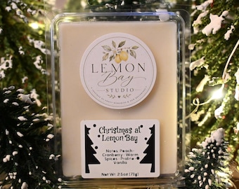 Könnte beinhalten: Ein rechteckiger, cremeweißer Wachsschmelzriegel in einer durchsichtigen Kunststoffverpackung. Das Etikett zeigt den Text Lemon Bay Studio und ein zweites Etikett trägt die Aufschrift Christmas at Lemon Bay, Notes Peach, Cranberry, Warm Spices, Praline, Vanilla, Net Wt 71g.