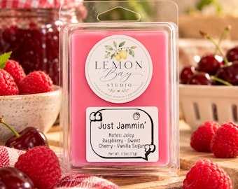 Könnte beinhalten: Ein rosafarbenes Duftwachs in einer durchsichtigen Kunststoffverpackung mit einem runden Lemon Bay Studio-Etikett und einem rechteckigen Aufkleber mit der Aufschrift Just Jammin' Notes: Juicy Raspberry, Sweet Cherry, Vanilla Sugar, 71g.