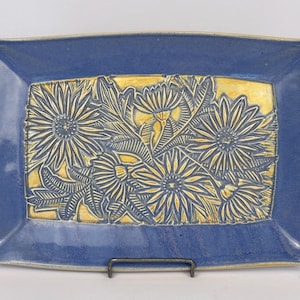 May include: A rectangular ceramic tray featuring a deep blue glazed border and a central panel with a yellow background. The centre displays a relief-carved floral pattern of dark blue flowers and leaves with intricate line details throughout.