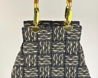 Peut inclure: Un sac à main structuré présentant un motif tressé de fibres bleu marine foncé et crème. Le sac possède une poignée supérieure arrondie en bois fixée au corps par des attaches en métal doré brillant.