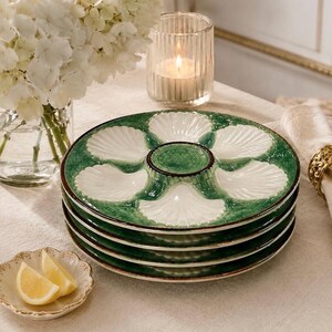 May include: A stack of four round ceramic oyster plates featuring a green textured border and six white shell-shaped indentations arranged around a central circular well. The plates have a glossy finish and a dark brown rim detail.