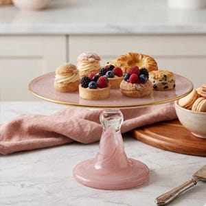 May include: A pink glass cake stand with a gold rim holds an assortment of pastries, including cream puffs, fruit tarts topped with fresh raspberries and blueberries, and a scone. The stand features a swirling pink pedestal base and a smooth surface.