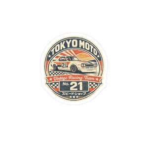 May include: A circular sticker featuring a white vintage race car with the number 21. The design includes the text TOKYO MOTO, Vintage Racing Team, No. 21, and Japanese characters. The colour palette consists of navy blue, red, and cream.
