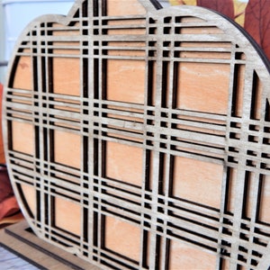 May include: A wooden pumpkin cutout with a plaid pattern. The pumpkin is painted a light brown color and has a dark brown plaid pattern.