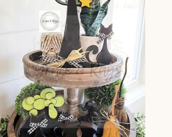 May include: A two-tiered wooden tray featuring Halloween-themed decor including a black witch hat with a yellow star, a black cat silhouette with a buffalo check bow, a small broom, a skull, and black boots. The text Grace & Rays is visible.