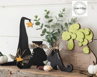 May include: A set of wooden Halloween decorations featuring a tall black witch hat with a yellow star, two black curled-toe boots with black and white gingham bows, and a brown cauldron with green bubbles and the word Wicked engraved on the front.