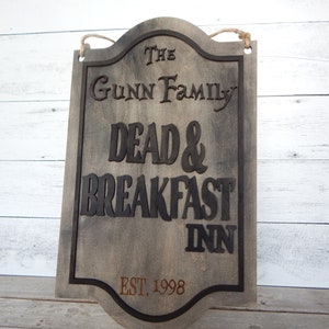 May include: A rustic wooden sign with black lettering that reads "The Gunn Family Dead & Breakfast Inn Est. 1998".