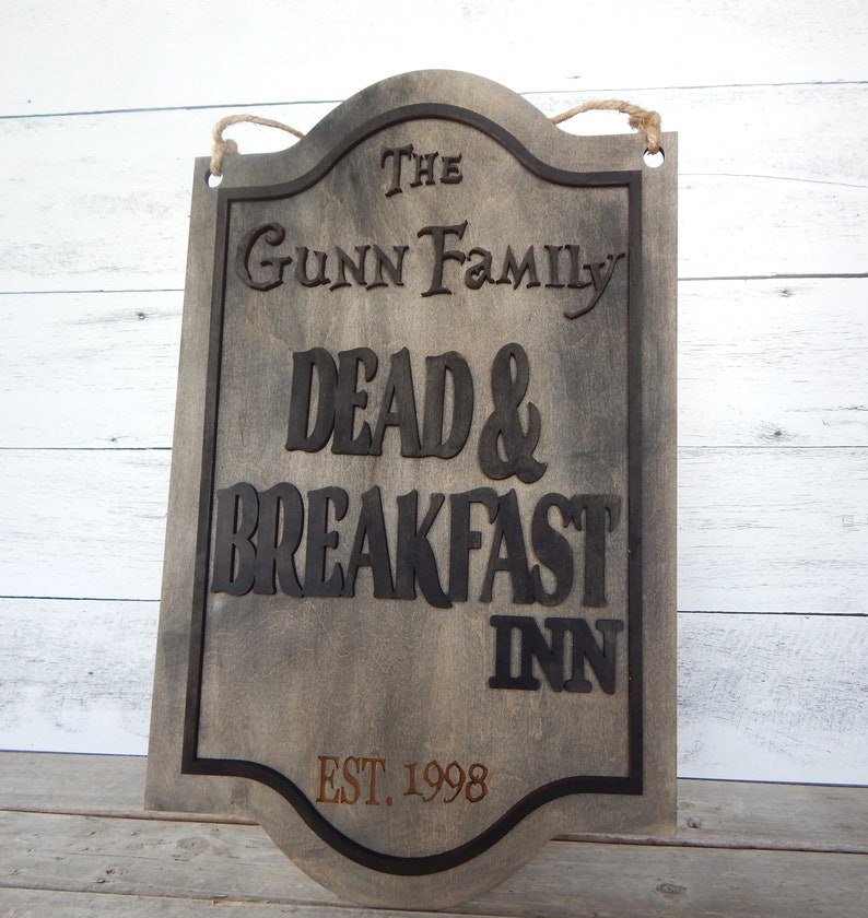 May include: A rustic wooden sign with black lettering that reads "The Gunn Family Dead & Breakfast Inn Est. 1998".