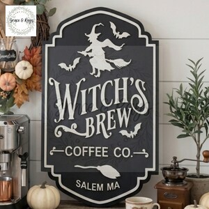 May include: A black and white decorative wall sign with a scalloped edge featuring a silhouette of a witch on a broomstick, bats, and the text Witch's Brew Coffee Co. Salem MA. The design includes a white broom icon at the bottom center.