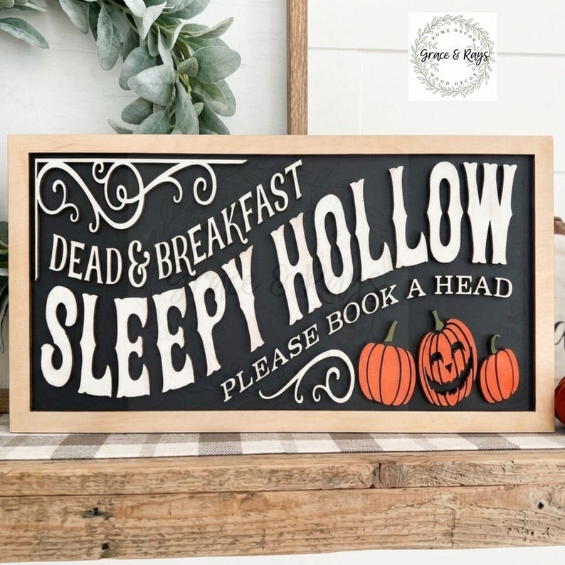 May include: A rectangular wooden sign with a light wood frame and a black background. The sign features white text that reads Dead & Breakfast Sleepy Hollow Please Book A Head, with white scrollwork and three orange pumpkins at the bottom right.