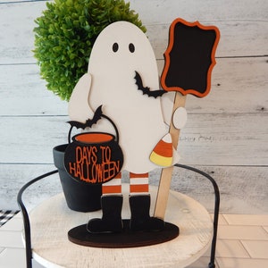 May include: A white ghost holding a black cauldron with the text "Days to Halloween" and a chalkboard sign. The ghost is wearing black boots and red and white striped legs. The ghost is standing on a wooden base.