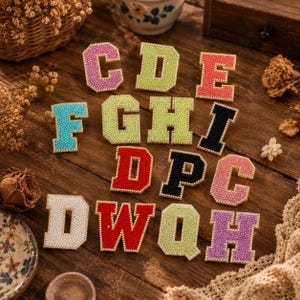 Peut inclure: Une collection d'écussons en forme de lettres style universitaire avec une finition en strass étincelants. L'ensemble comprend diverses lettres aux couleurs vives comme rose, vert lime, corail, turquoise, noir, rouge et blanc, bordées d'or.