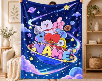May include: A dark blue fleece blanket featuring a space-themed design with colourful cartoon characters, stars, and planets. The word NAME is printed in large, multi-coloured bubble letters across a central planet graphic surrounded by clouds.