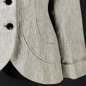 Puede incluir: Una chaqueta gris con cierre de un solo botón y un diseño de bolsillo curvo único. La chaqueta tiene mangas largas con puños abotonados.