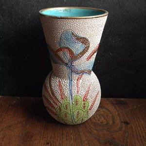 Op de afbeelding: Een decoratieve vaas met een getextureerd, gebroken wit oppervlak. De vaas heeft een blauw interieur, een gouden rand en een ontwerp van blauwe, rode en groene bloemelementen. De vaas heeft een bolvormige basis en een uitlopende bovenkant.