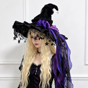 May include: A black witch hat featuring a wide, ruffled brim adorned with dangling black star and moon charms. The hat includes a vibrant purple organza ribbon bow, black lace trim, and a small gold star charm hanging from the pointed top.