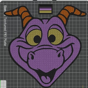 May include: An embroidered patch featuring a purple dragon head with large yellow eyes, orange horns with black stripes, and a wide smiling mouth. The design is outlined in thick black thread and set against a dark gray grid background.