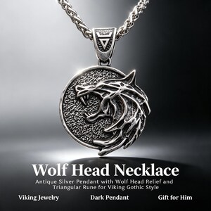 May include: A silver-toned metal necklace featuring a circular pendant with a detailed wolf head relief. The pendant is attached to a textured triangular bail and hangs from a thick, braided silver chain. The surface has an oxidized finish.