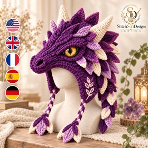 Può includere: Un cappello all'uncinetto a forma di drago nei toni del viola, lavanda e crema, caratterizzato da un motivo a scaglie testurizzato, un muso prominente e un grande occhio giallo con pupilla a fessura nera. Due paraorecchie intrecciati terminano a foglia.