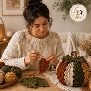 Female crochet artisan crocheting a rust-colored oak-leaf coaster beside the completed woodland pumpkin and coordinated cotton yarn.