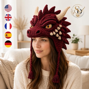 Può includere: Un cappello all'uncinetto a forma di drago rosso scuro con squame testurizzate, due corna beige e occhi gialli realistici. Il cappello include paraorecchie con nappe intrecciate che pendono su ogni lato, imitando una testa di drago con muso.