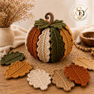 Crochet leaf pumpkin displayed in a warm neutral home setting, showing raised oak-leaf panels, olive crown leaves, curled brown stem and autumn color palette.