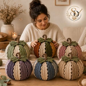Six finished crochet leaf pumpkins displayed together in autumn, sage, pink, purple, blue and neutral color variations with the artisan behind them.
