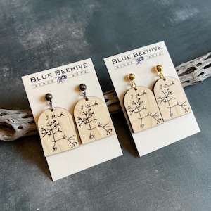 May include: Two pairs of wooden earrings with a light wood finish. Each earring features a black tree-like graphic and the handwritten text "I think". The earrings are displayed on white cards with the text "BLUE BEEHIVE SINCE 2012". One pair has silver-colored posts, the other gold.