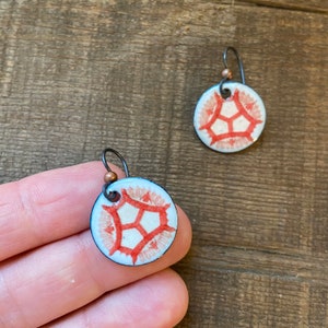 May include: A pair of earrings with a white background and a red geometric design. The earrings are made of metal and have a hook closure.