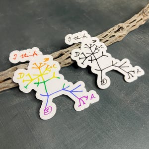 May include: Two white stickers with a tree-like diagram and the handwritten text "I think". One sticker features a rainbow-colored diagram, while the other is black and white. The stickers are placed on a dark surface with a dried branch.