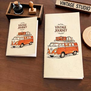 May include: Two cream-colored notebooks featuring a brown illustration of an orange van with luggage on the roof and the text VINTAGE JOURNEY. The notebooks are displayed with a wooden tray containing a glass ink bottle and a wooden stamp.