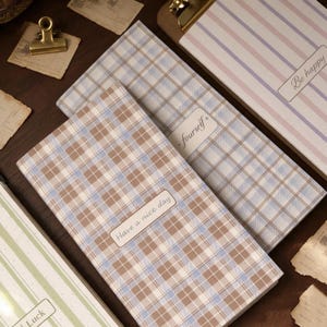 May include: Three rectangular notebooks with varied patterns. One features a brown and blue plaid design with the text "Have a nice day". Another has a blue and white plaid pattern with the text "fourself". A third has green stripes and "Luck".